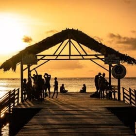 Photo by Kenrick Baksh: https://www.pexels.com/photo/silhouette-of-people-standing-on-a-thatched-roof-jetty-during-sunset-5376665/